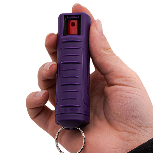 Hand holding a purple pepper spray device with a white background