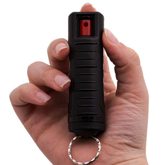 Hand holding a black pepper spray device with a red component on a white background